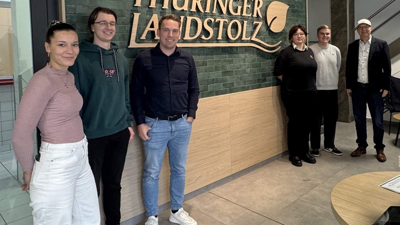 Zu Besuch bei Thüringer Landstolz: Alle Beteiligten vor dem Logo-Schriftzug im Eingang der Fleisch- und Wurstwaren Schmalkalden GmbH Thüringen