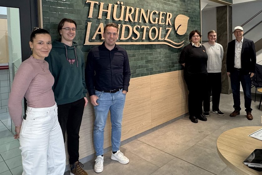 Zu Besuch bei Thüringer Landstolz: Alle Beteiligten vor dem Logo-Schriftzug im Eingang der Fleisch- und Wurstwaren Schmalkalden GmbH Thüringen