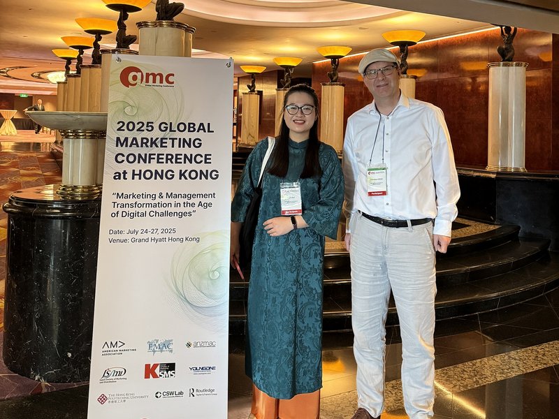 Prof. Dr. Sebastian Ullrich und Phuong Thanh Bui vor einem Banner der Global Marketing Conference in Hongkong