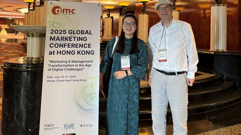Prof. Dr. Sebastian Ullrich und Phuong Thanh Bui vor einem Banner der Global Marketing Conference in Hongkong