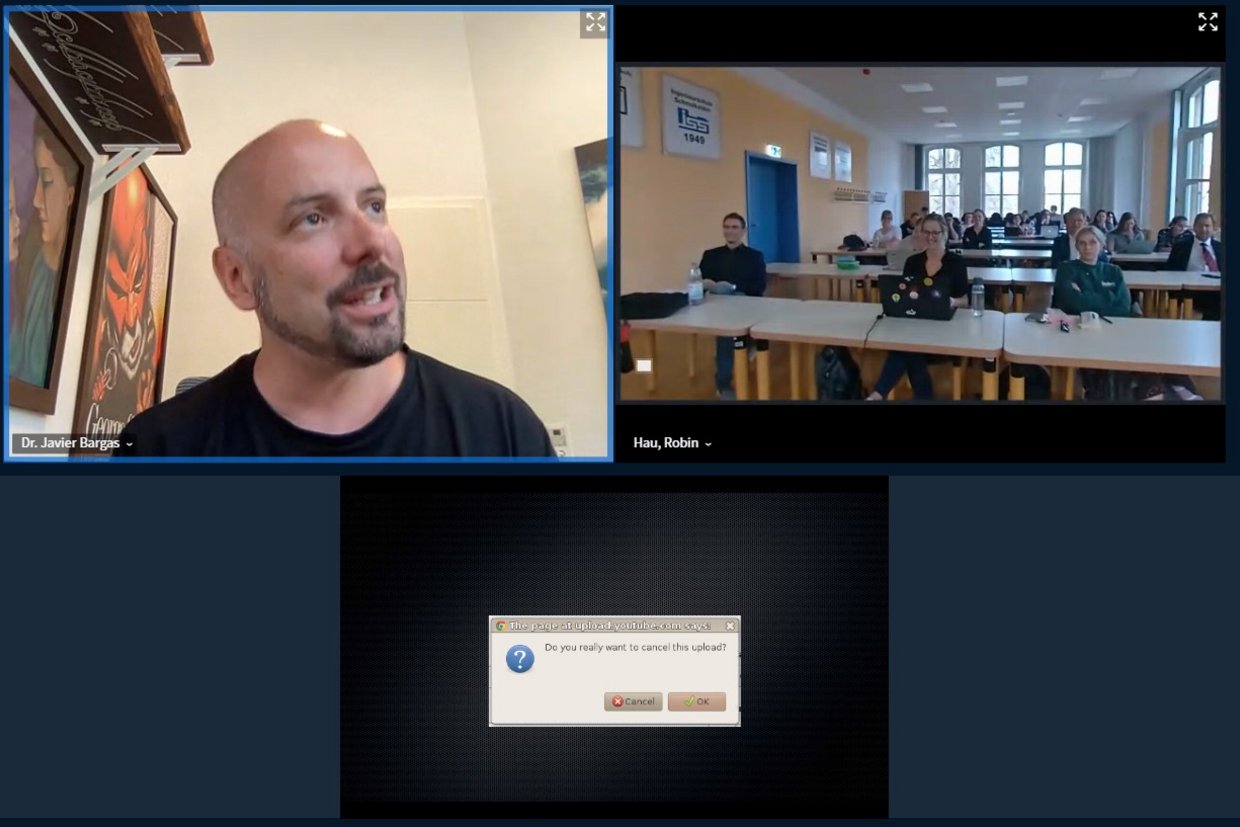 Links oben wird ein Fenster mit dem zugeschalteten Herrn Dr. Bargas gezeigt, rechts oben ein Fenster mit den Teilnehmenden in der Aula. Unten findet sich ein Fenster in der Mitte mit dem Text: "Do you really want to cancel the upload? Cancel/OK".