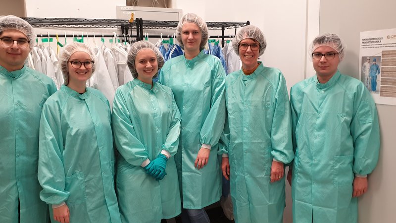 Gruppenfoto: Frau Prof. Dr. Störmann mit Studierenden im Produktionsbereich der Opvius GmbH. Alle tragen helle Schutzkleidung und Haarnetz.