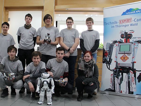 Schülergruppe vor einem Poster mit Roboter und einem kleinem Roboter im Vordergrund
