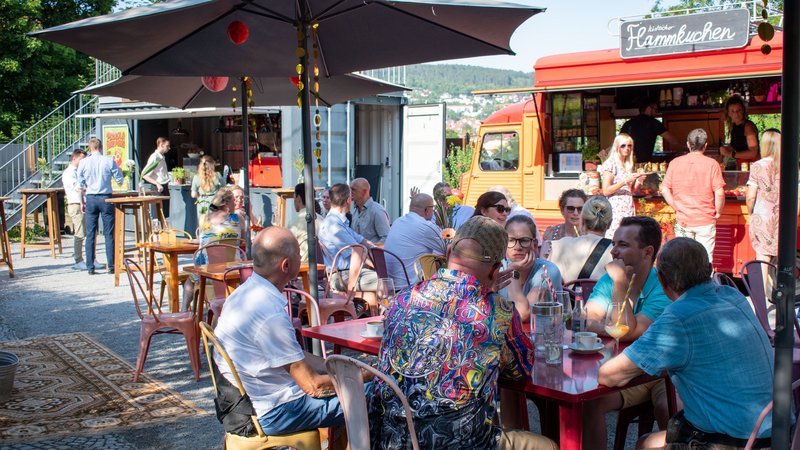 Menschen sitzen an Tischen unter Sonnenschirm