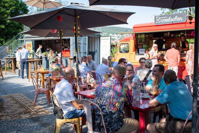 Menschen sitzen an Tischen unter Sonnenschirm