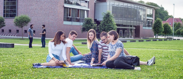 Studierende auf der Wiese vor dem H-Gebäude