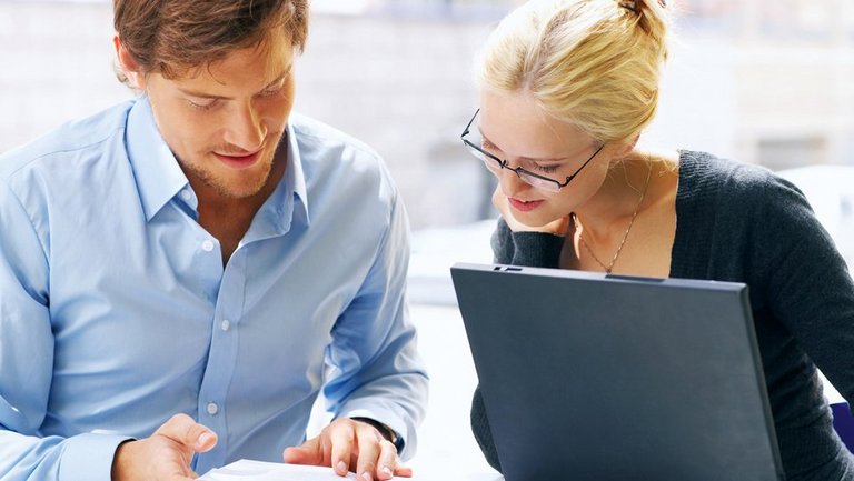 Mann und Frau vor einem Buch und einem Laptop