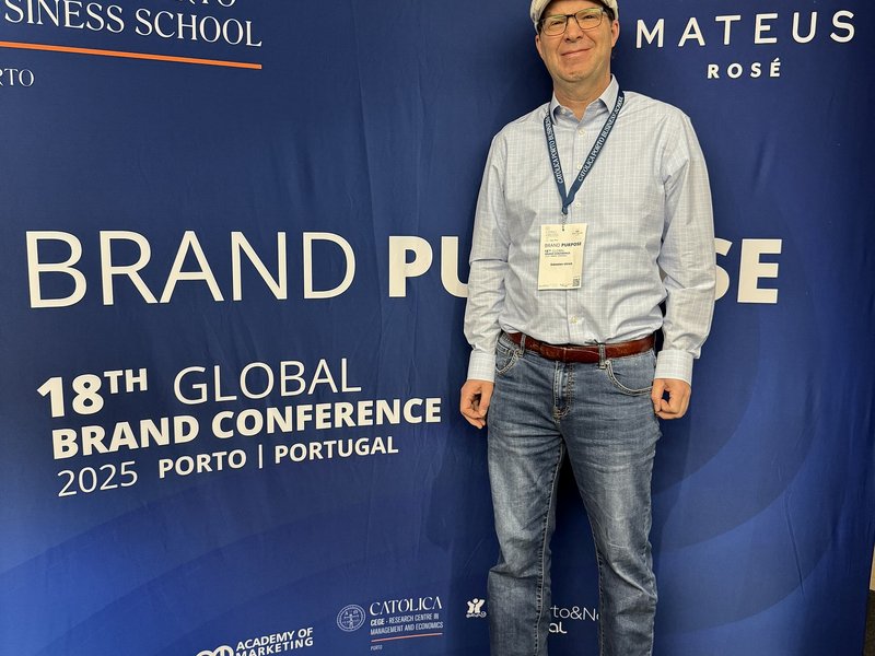Prof. Dr. Sebastian Ullrich vor einem Banner der Global Brand Conference in Porto, Portugal