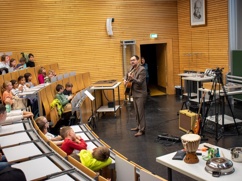 Professor spielt Gitarre vor Kindern