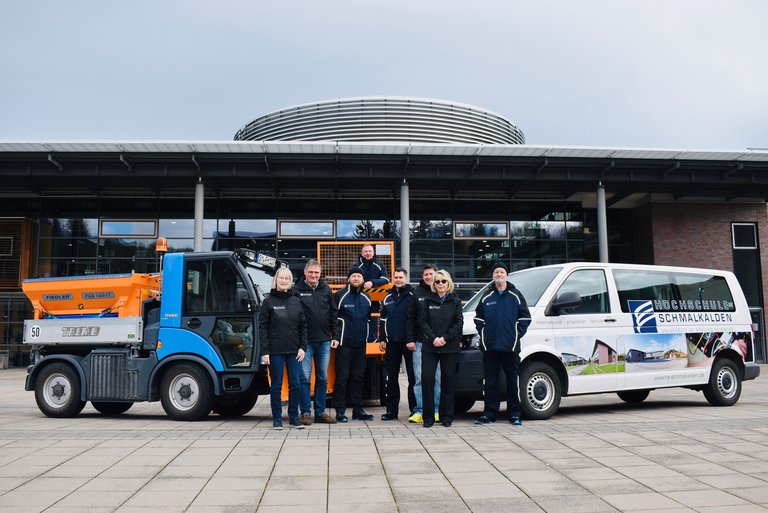 Menschen vor Fahrzeugen vor der Hochschule 