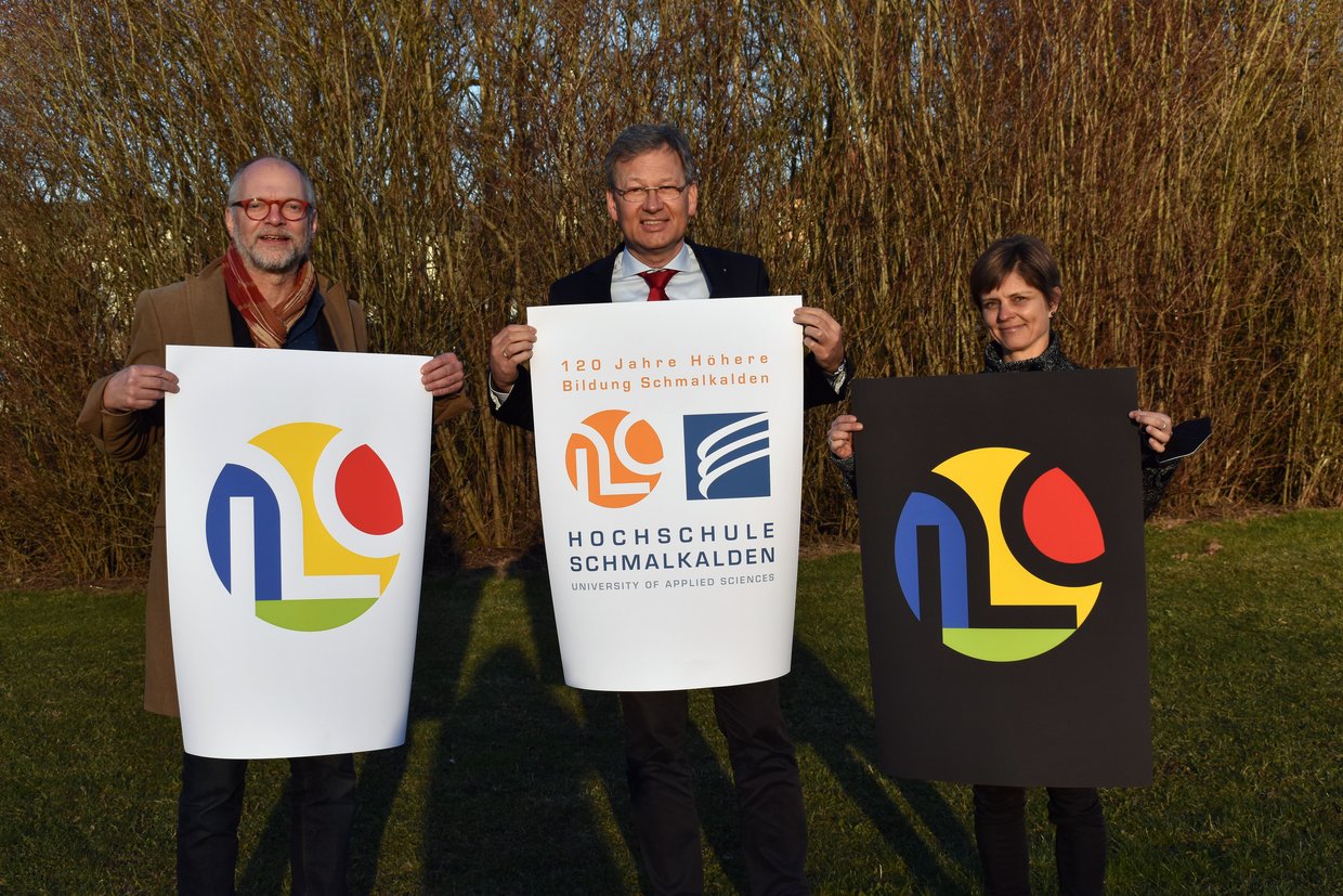 Grafikprofessor Joachim Dimanski, Hochschulpräsident Prof. Gundolf Baier und Pressesprecherin Ina Horn mit dem Jubiläumslogo