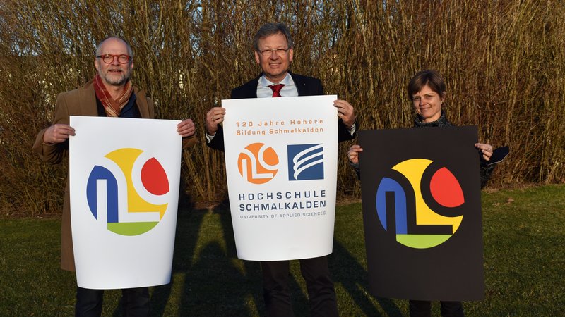 Grafikprofessor Joachim Dimanski, Hochschulpräsident Prof. Gundolf Baier und Pressesprecherin Ina Horn mit dem Jubiläumslogo