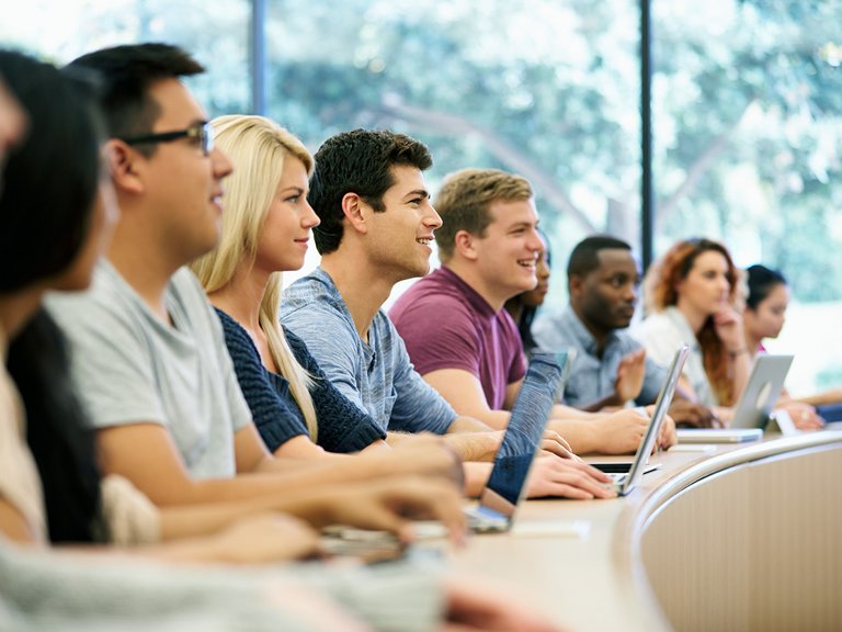 Alumni in einem Hörsaal mit Arbeitsgeräten wie sie einer Vorlesung lauschen