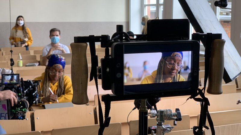 1) Drehszene im Hörsaal C101, Blick auf den Kameramonitor und in den Hörsaal: Hauptdarstellerin im Fokus, zwei Komparsen im Hintergrund