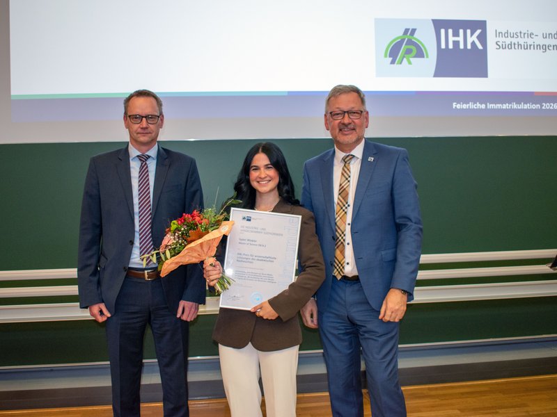 Drei Personen mit Urkunde und Blumen