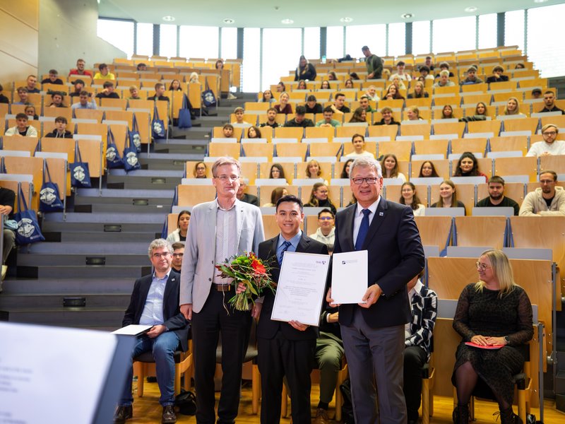 Student und zwei Männer mit Urkunde